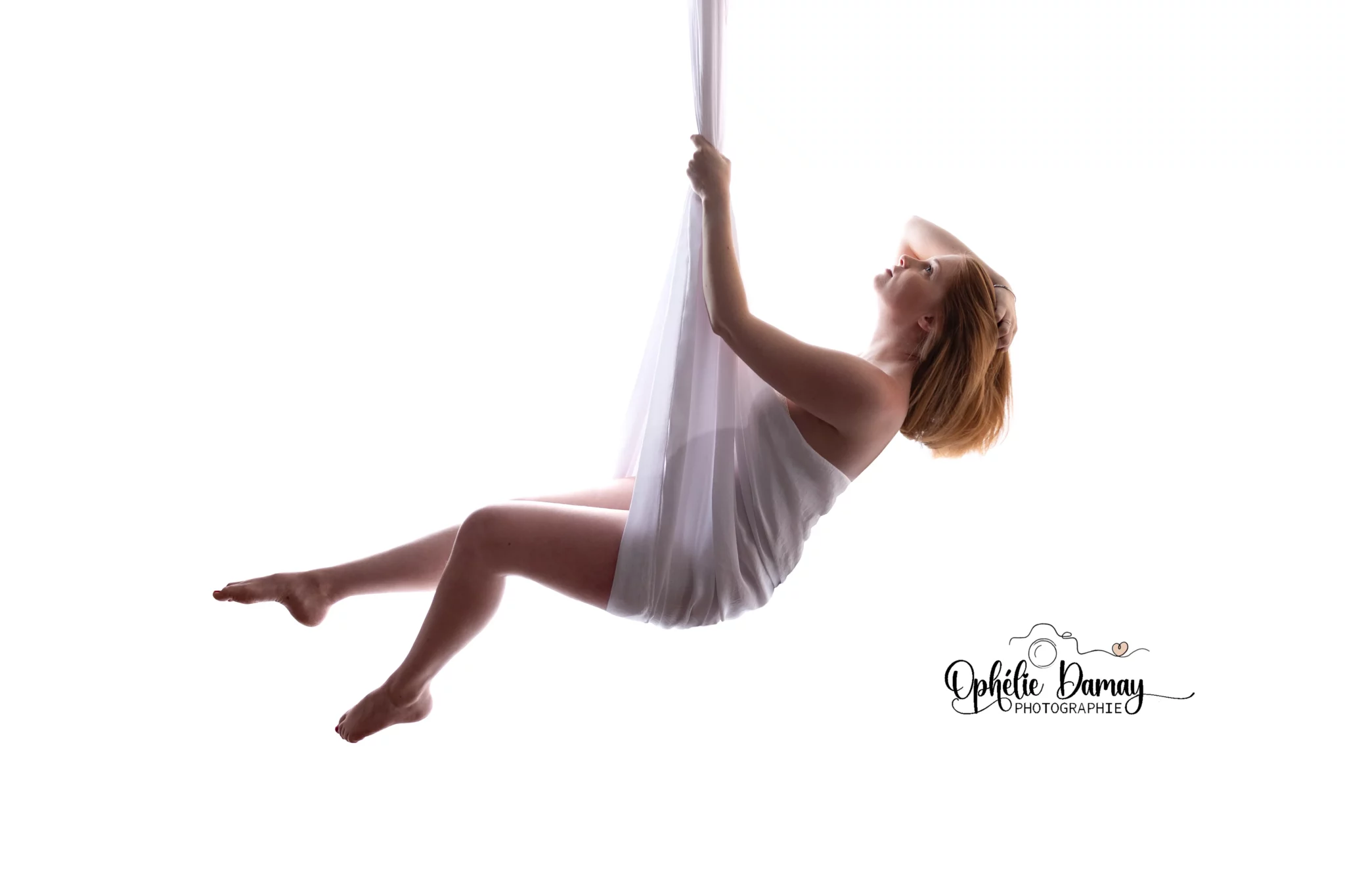 alt="Femme enceinte suspendue dans un voilage blanc, sensation de douceur et de légèreté"