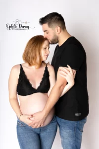 alt="Couple attendant un bébé. L'homme embrasse tendrement sa femme sur le front."