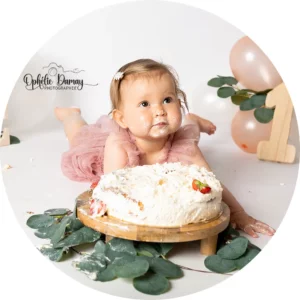 alt="Bébé allongé sur le ventre, devant un gâteau, lors d’une séance photo à Hargnies"
