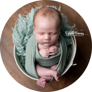 alt="Portrait de nouveau-né emmailloté, posé dans un panier, studio photo à Hargnies"