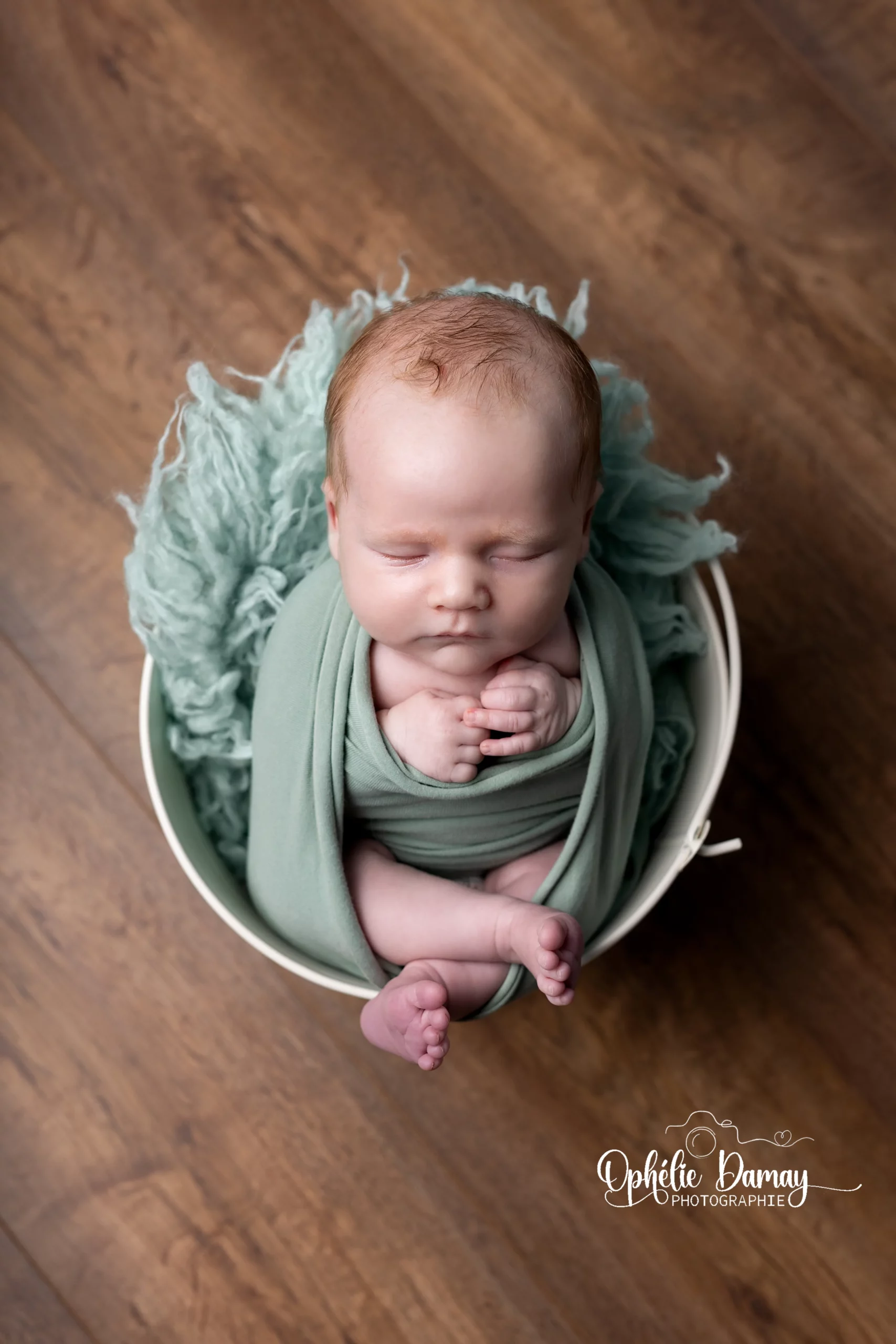 alt="Photo de nouveau-né emmailloté dans un panier, lumière douce en studio photo"