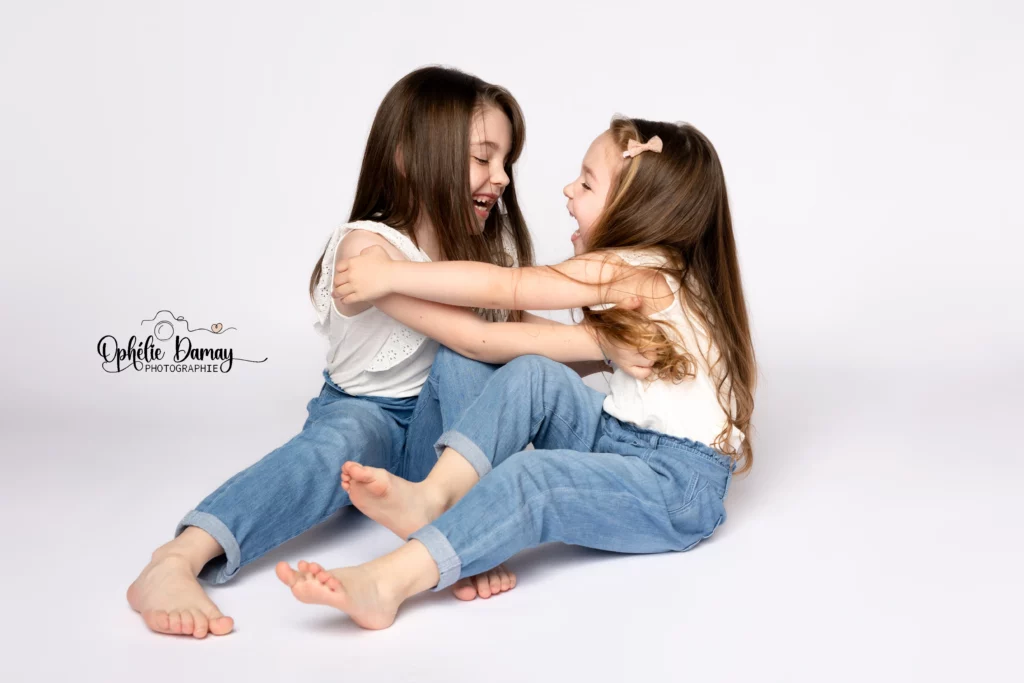 alt="Deux sœurs riant ensemble pendant une séance photo en studio"