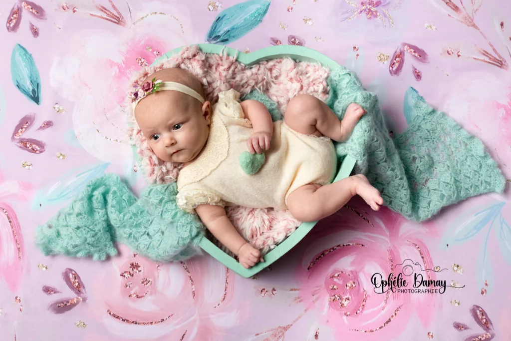 alt="Nouveau-né dans un coeur, sur un décor fleuri et coloré"