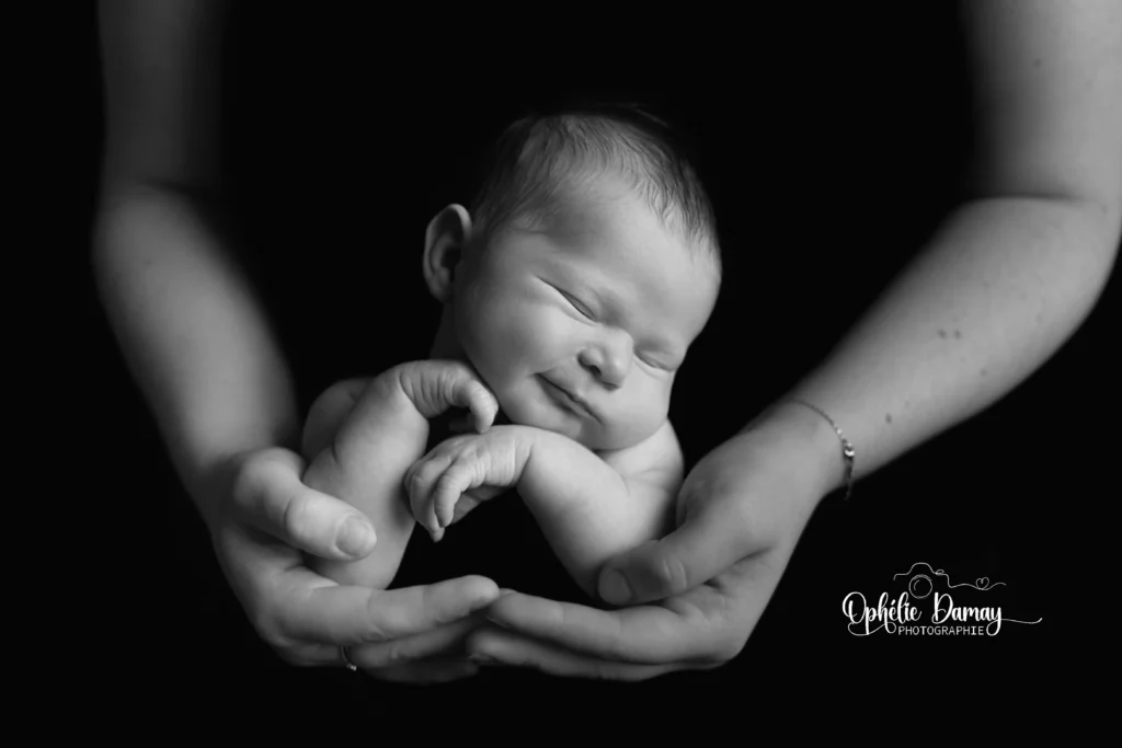 alt="cliché d'un nouveau-né appuyé sur ses mains, avec les mains de sa maman apparentes"