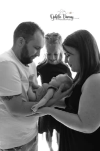 alt="Parents et grande soeur tenant leur nouveau-né avec tendresse pendant une séance naissance"