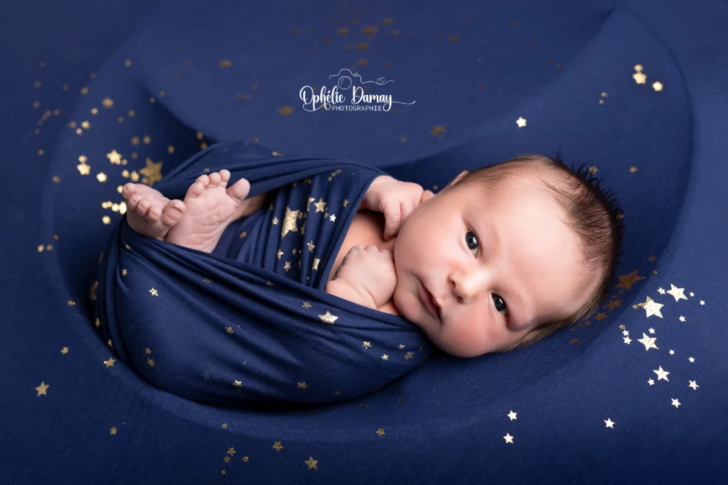 alt="Nouveau-né emmailloté et allongé dans un contenant en forme de lune, entouré d'étoiles"