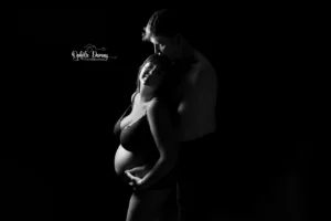alt="cliché d'un couple attendant un bébé, en noir et blanc avec un jeu de lumière ne montrant que les courbes du couple"