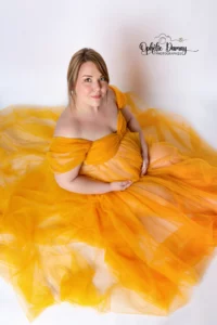 alt="Cliché d'une femme enceinte, assise au sol, dans une robe volumineuse, prise en plongée"