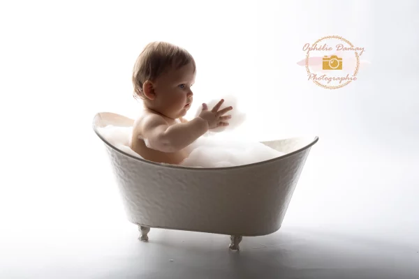alt="Bébé dans un bain rempli de mousse, lumière douce"