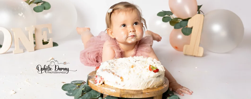 alt="bébé fêtant ses 1 an, et mangeant son gâteau tout seul en s'en mettant partout"